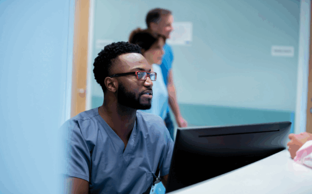 Male health worker looking at computer screen at reception desk.