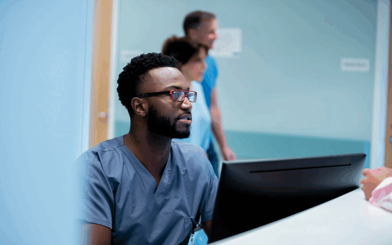 Male health worker looking at computer screen at reception desk.
